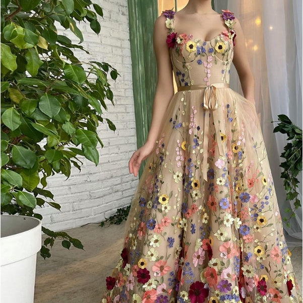 Beige evening gown with floral embellishments in a room with plants and white brick wall.