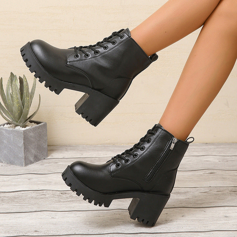 Black leather boots with chunky soles worn by a person on a wooden floor.