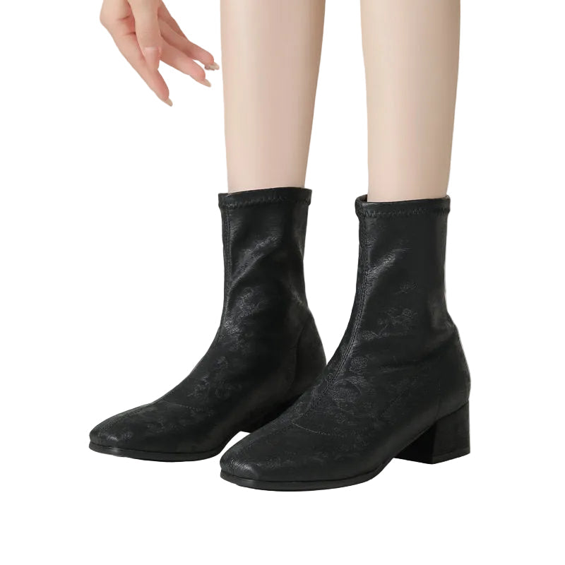 Black leather ankle boots worn by a person on a neutral background