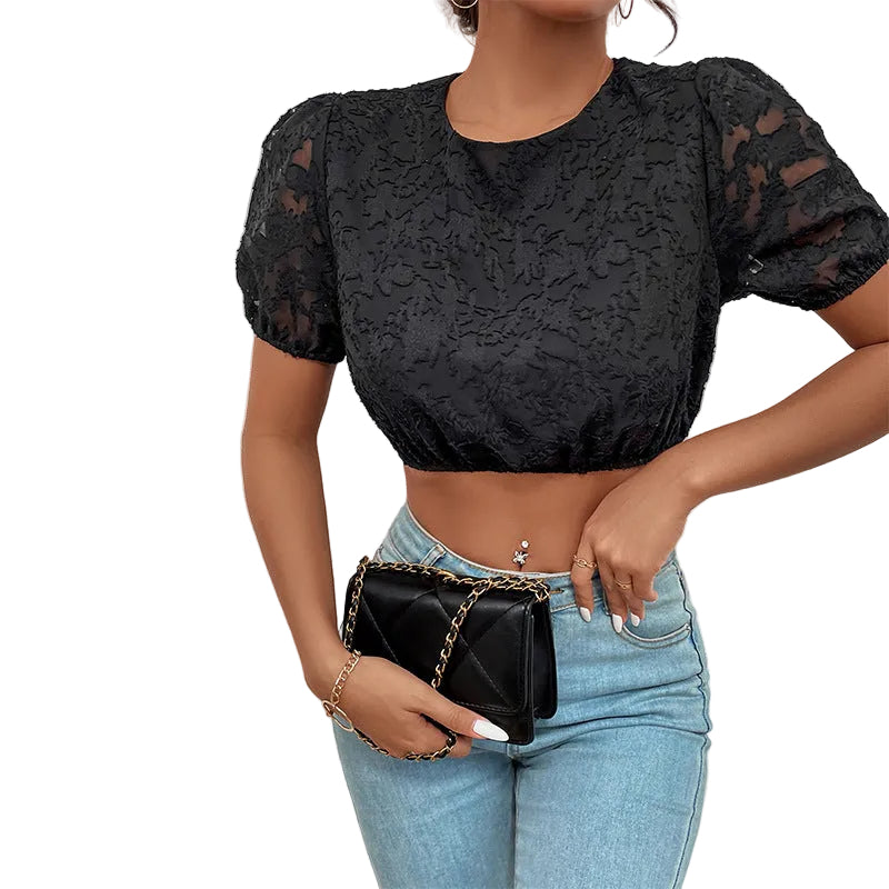 Person wearing a black lace top and blue jeans, holding a black handbag against a white wall.