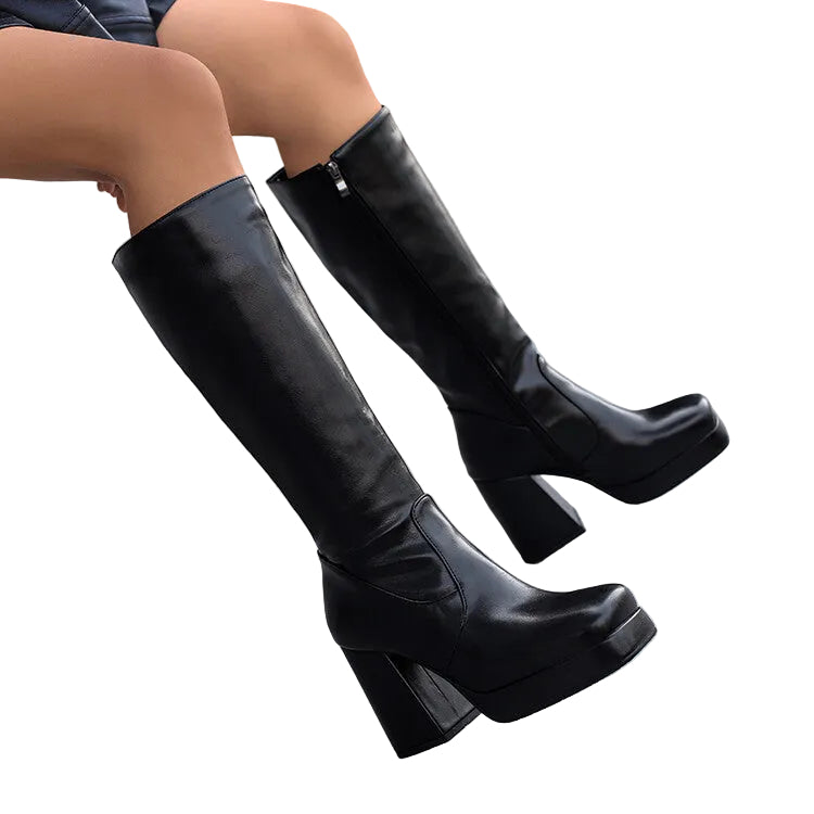 Black knee-high boots with chunky heels worn by a person sitting on a chair.